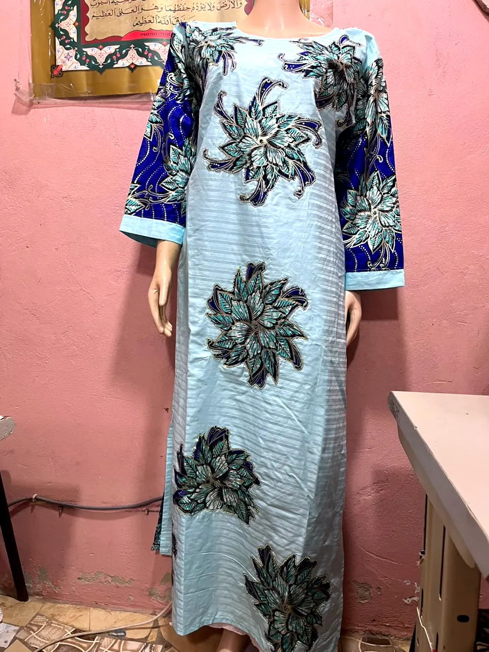 Robe longue bleu ciel décorée de grandes fleurs bleu et turquoise, manches bleu roi, présentée sur mannequin