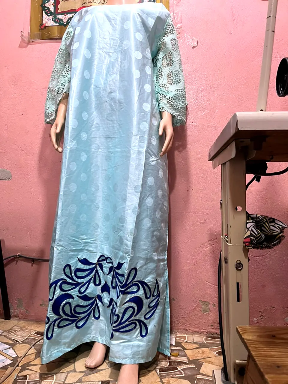 Robe longue turquoise pâle avec manches ajourées et broderie bleu roi en bas, présentée sur mannequin