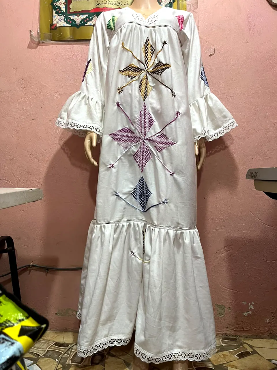 Robe longue blanche à broderies géométriques multicolores et bordures en dentelle, présentée sur mannequin